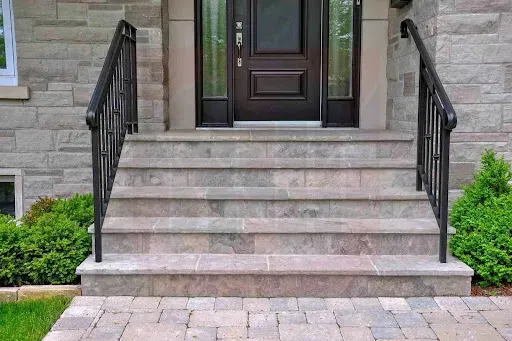 Stone steps leading to a black door with wrought iron railings and shrubs on either side