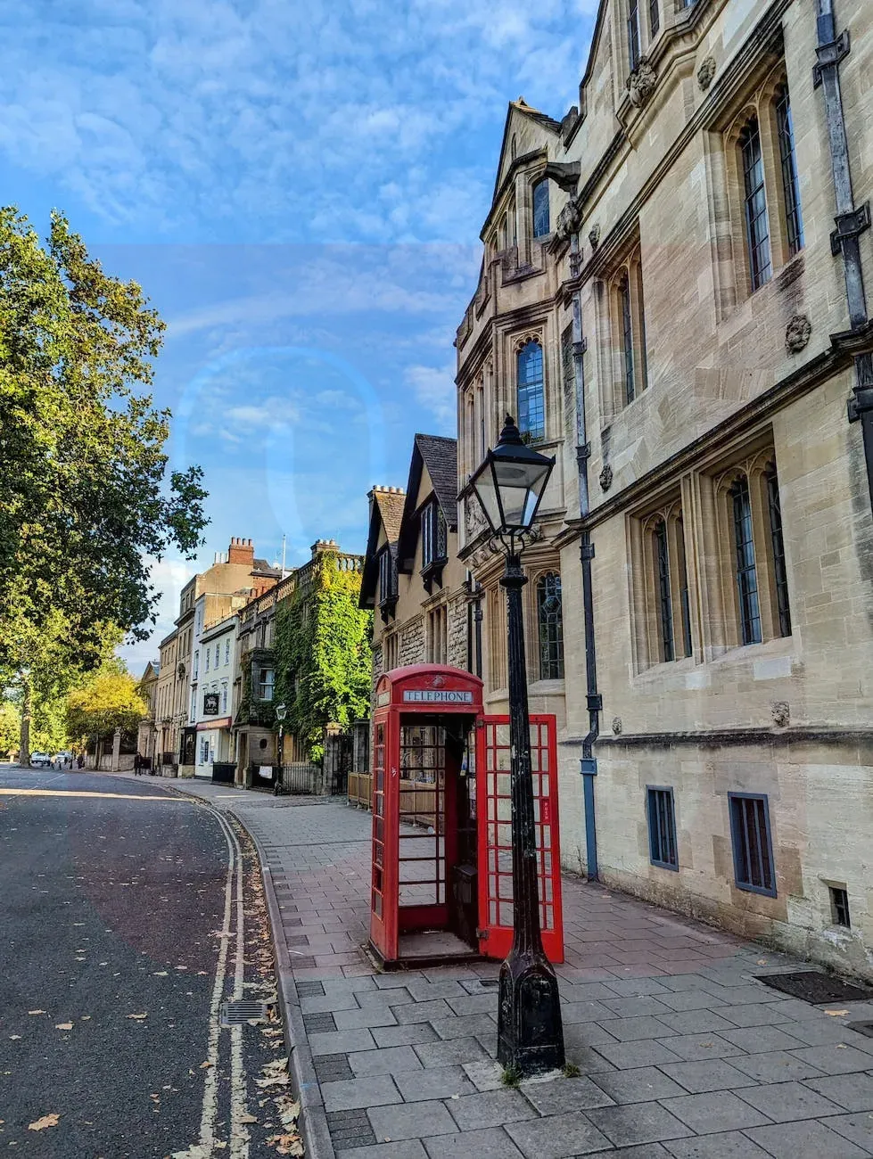 Red telephone booth on a clean, wide sidewalk next to historic stone buildings, with smooth paving and ample pedestrian space