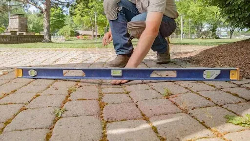 Worker using a level to check the evenness of a stone patio surface, ensuring proper alignment and stability of the pavers