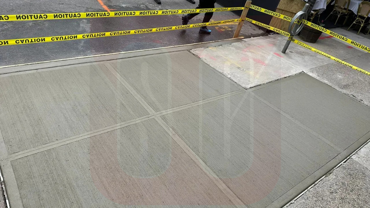 Fresh concrete being poured for a new sidewalk, with caution tape marking off the wet area
